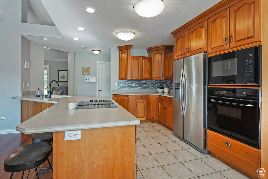 Kitchen with black appliances, decorative backsplash, light tile patterned flooring, kitchen peninsula, and a kitchen breakfast bar