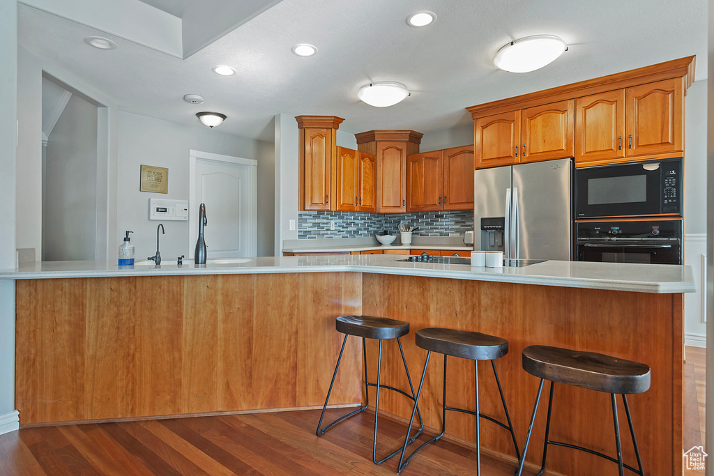 Kitchen featuring hardwood / wood-style flooring, sink, kitchen peninsula, and black appliances