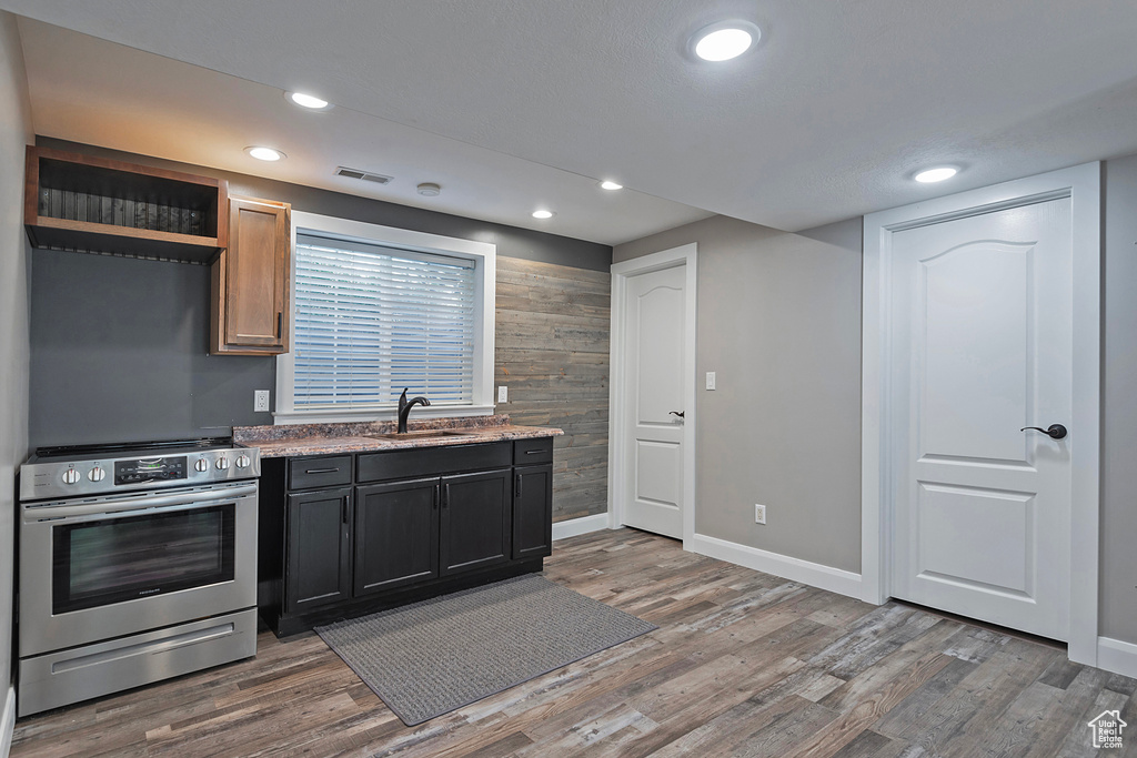 Kitchen featuring wood-type flooring, stainless steel electric stove, light stone countertops, and sink