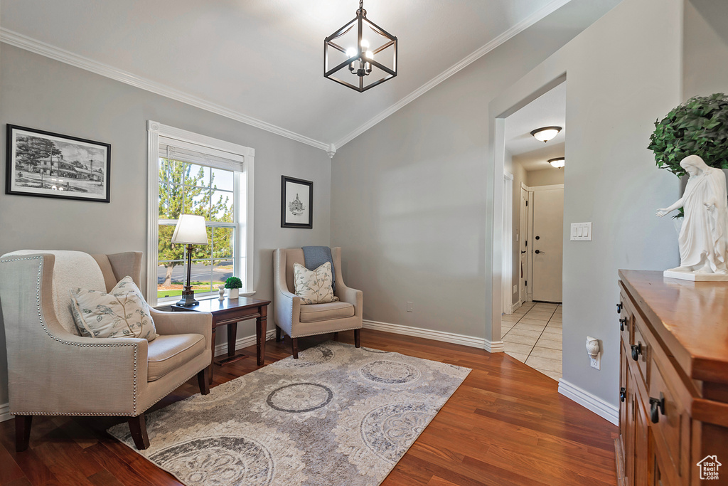 Sitting room with lofted ceiling, a notable chandelier, ornamental molding, and hardwood / wood-style flooring