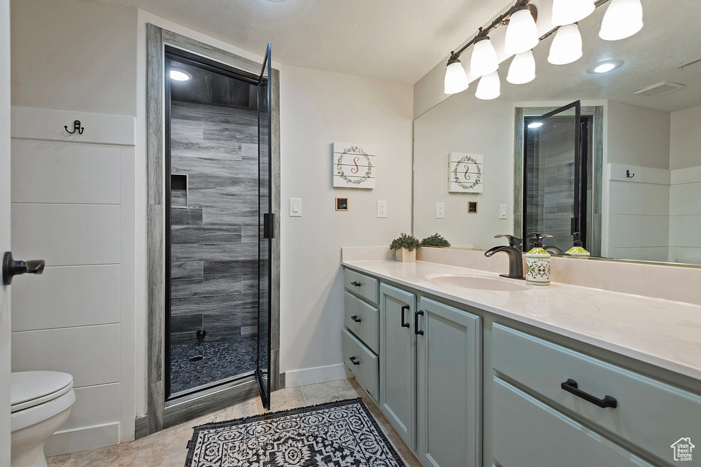 Bathroom featuring tile patterned flooring, a shower with door, vanity, and toilet