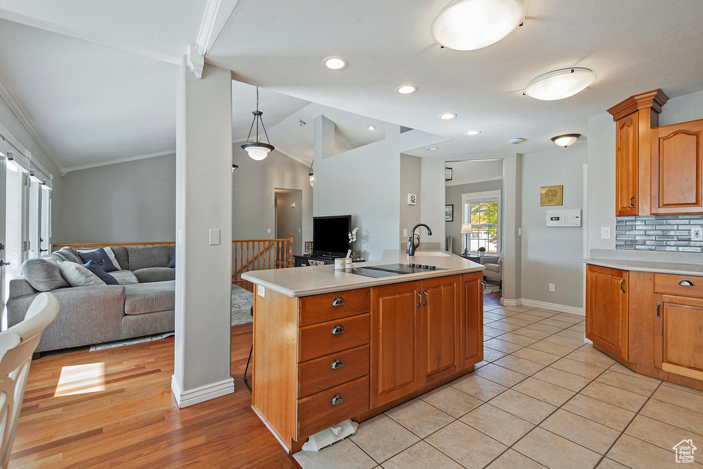 Kitchen featuring crown molding, a center island with sink, vaulted ceiling, hanging light fixtures, and light tile patterned floors