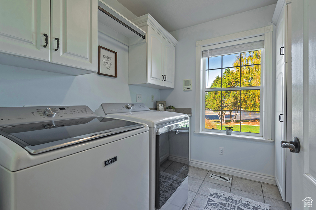 Clothes washing area with separate washer and dryer, cabinets, and light tile patterned floors