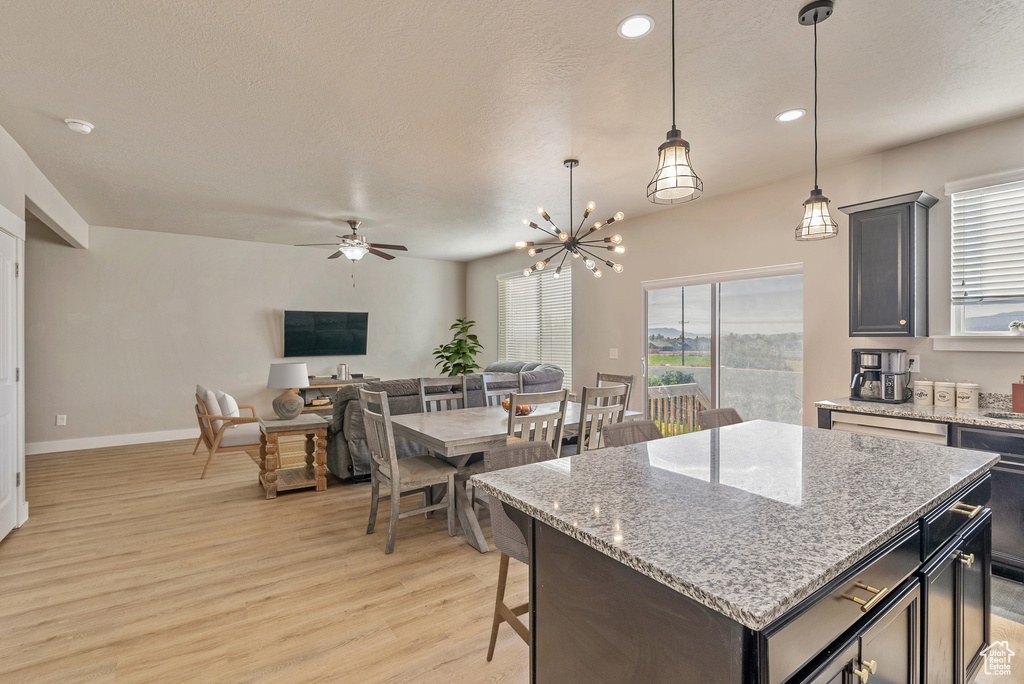 Kitchen with hanging light fixtures, ceiling fan with notable chandelier, a center island, light stone countertops, and light hardwood / wood-style floors