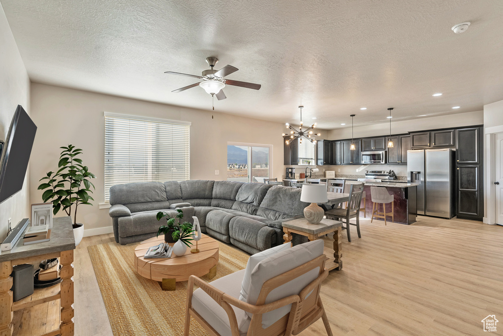 Living room featuring ceiling fan with notable chandelier, a textured ceiling, light wood-type flooring, and sink