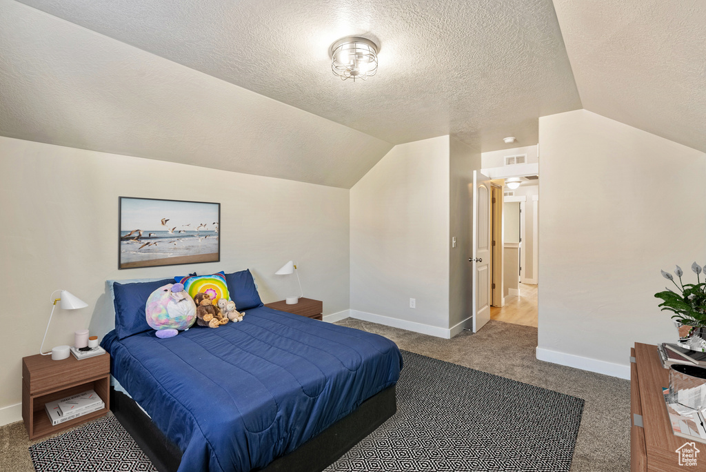 Bedroom featuring carpet floors, vaulted ceiling, and a textured ceiling