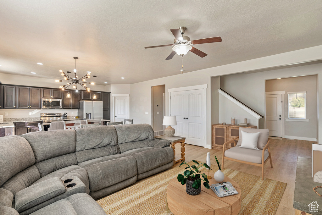 Living room featuring ceiling fan with notable chandelier, a textured ceiling, and light hardwood / wood-style flooring