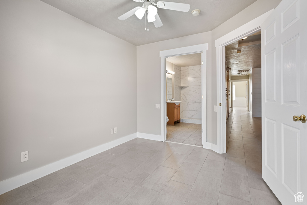 Unfurnished bedroom featuring light tile patterned flooring, ensuite bath, and ceiling fan