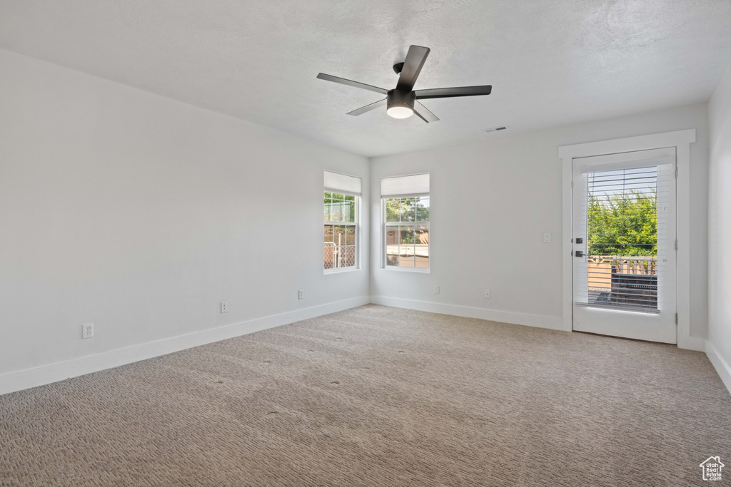 Unfurnished room featuring ceiling fan, light carpet, and a wealth of natural light