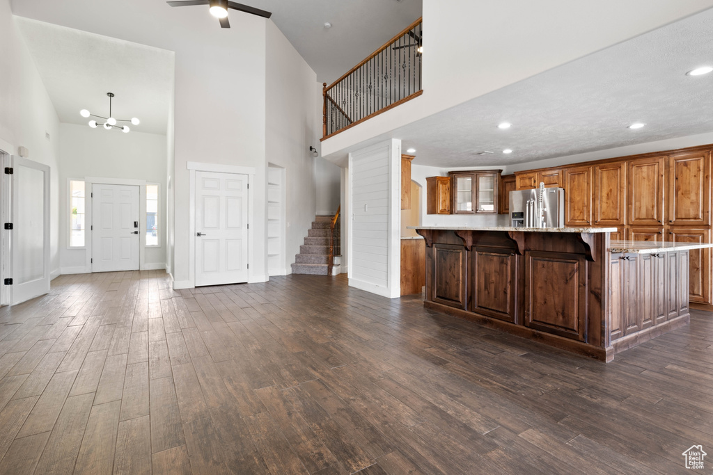 Kitchen featuring a breakfast bar, dark wood-type flooring, a towering ceiling, a large island, and stainless steel refrigerator with ice dispenser