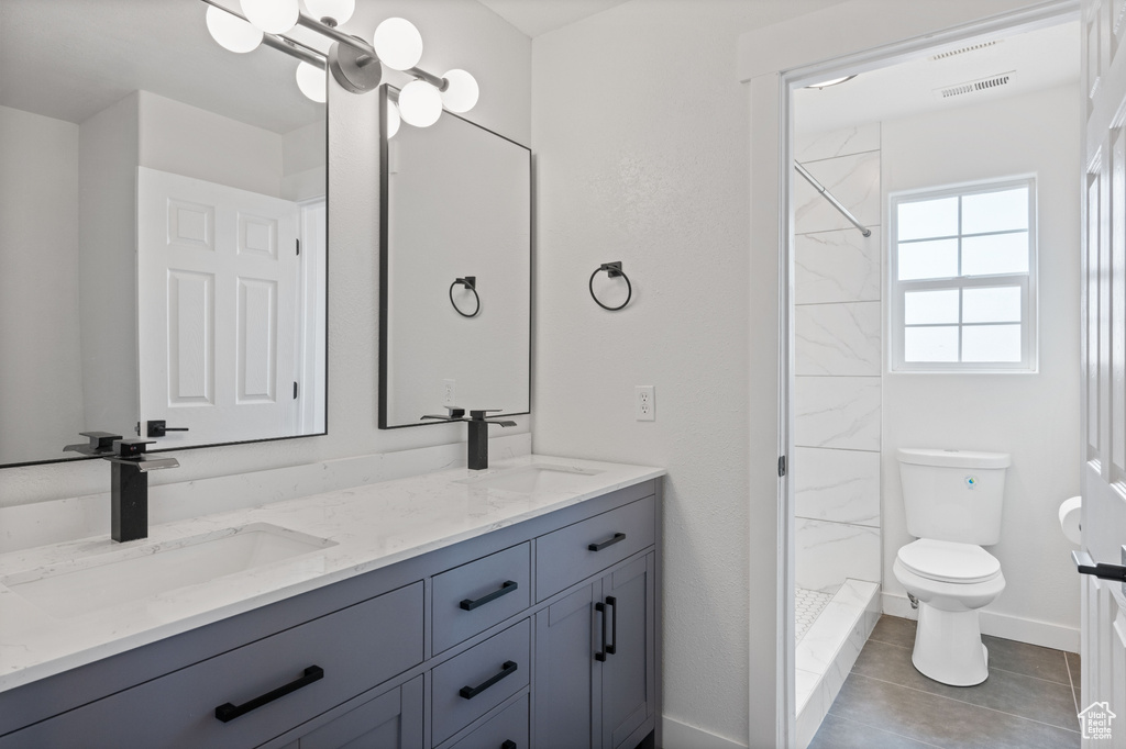 Bathroom featuring tile patterned flooring, vanity, tiled shower, and toilet