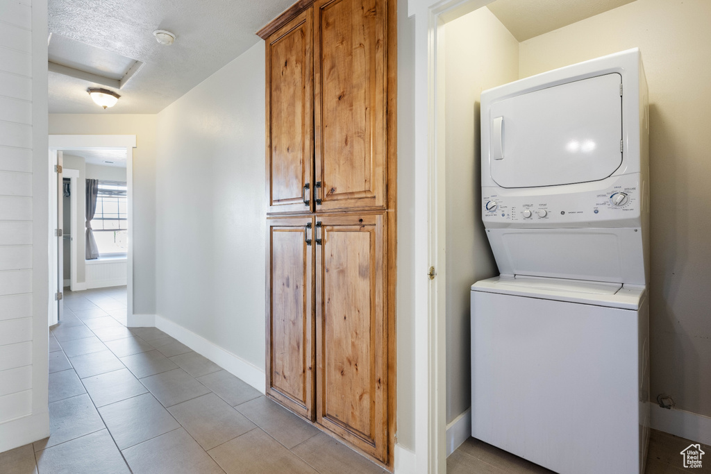 Clothes washing area featuring light tile patterned floors, stacked washer / drying machine, and a textured ceiling