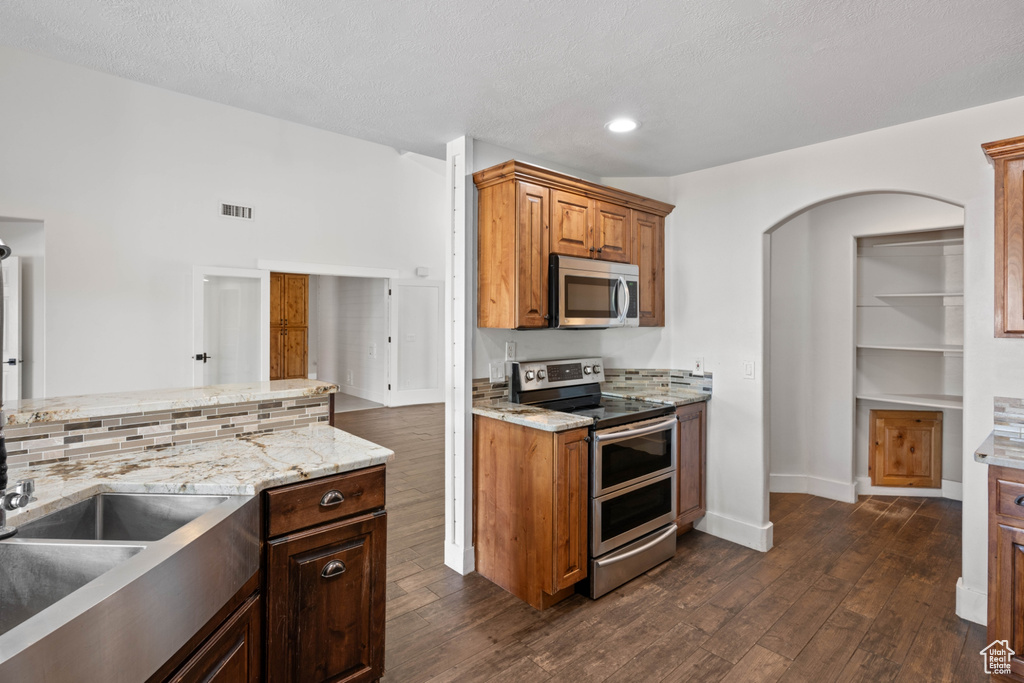 Kitchen with dark hardwood / wood-style flooring, sink, light stone countertops, appliances with stainless steel finishes, and a textured ceiling