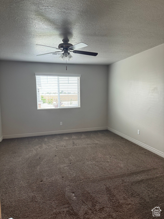 Empty room with ceiling fan, dark carpet, and a textured ceiling