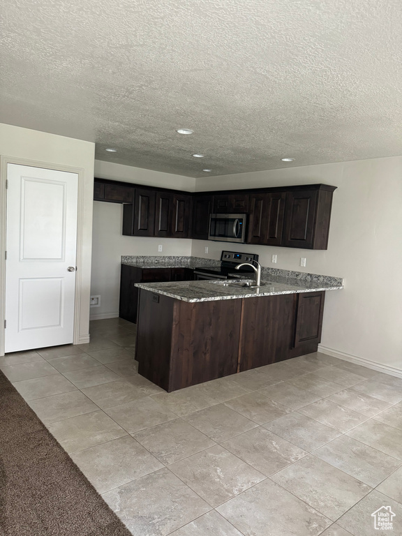 Kitchen featuring appliances with stainless steel finishes, kitchen peninsula, dark brown cabinetry, and a textured ceiling