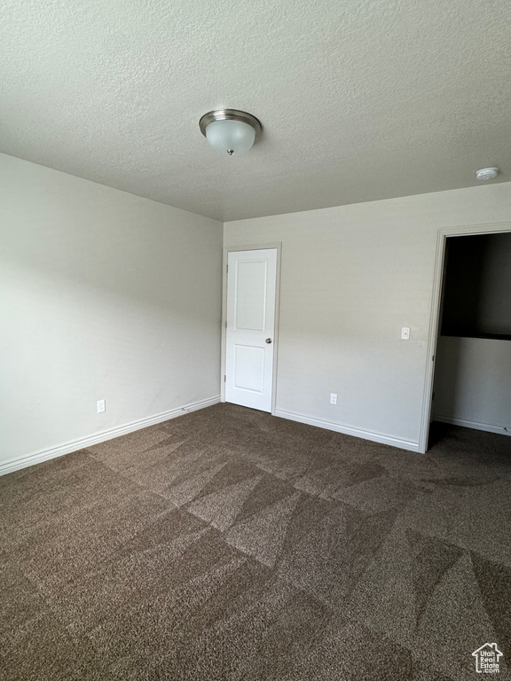Unfurnished room featuring dark carpet and a textured ceiling