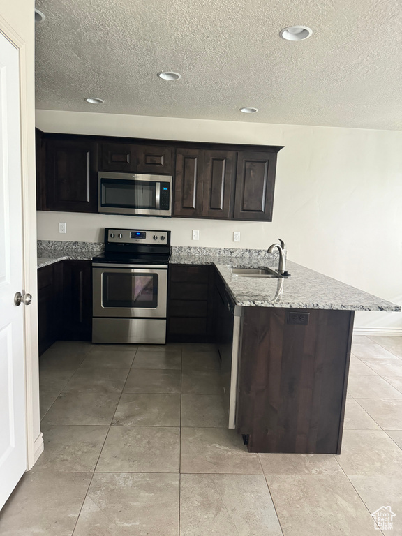 Kitchen with sink, kitchen peninsula, a textured ceiling, stainless steel appliances, and light stone countertops