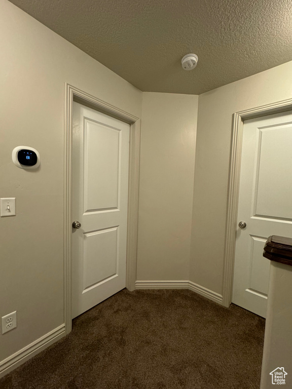 Hall with a textured ceiling and dark colored carpet