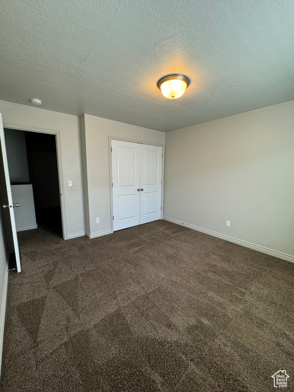 Unfurnished bedroom with dark carpet and a textured ceiling