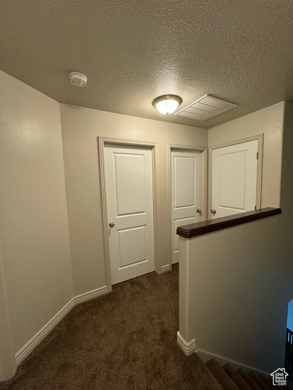 Hallway featuring dark carpet and a textured ceiling