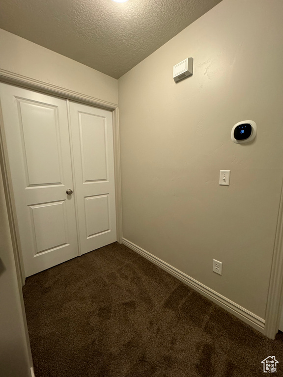 Interior space with a closet, dark carpet, and a textured ceiling