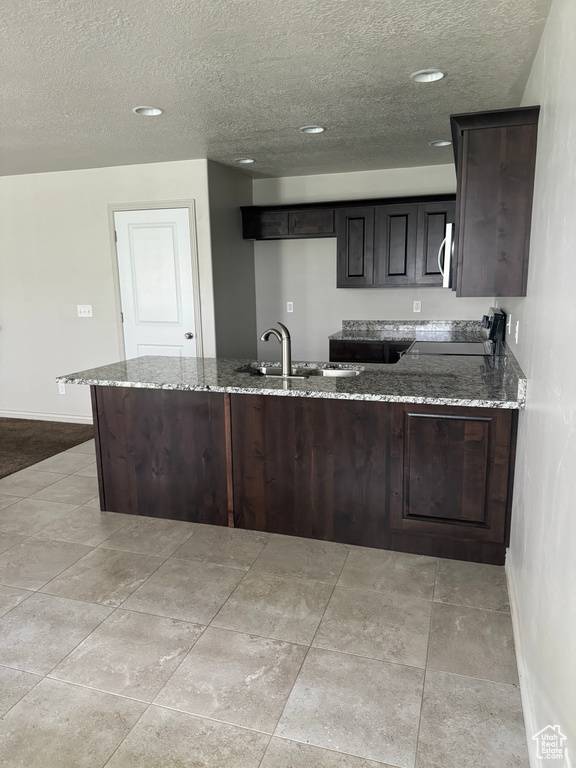 Kitchen featuring kitchen peninsula, light stone countertops, and sink