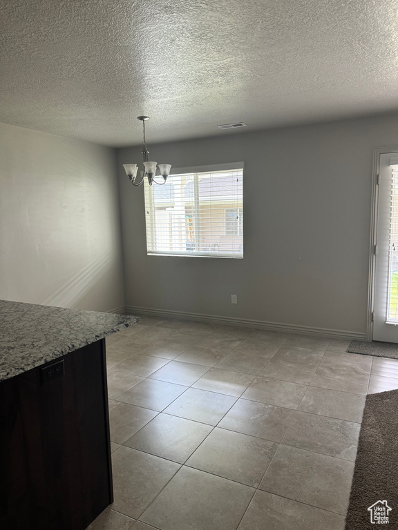 Unfurnished dining area with light tile patterned floors, a textured ceiling, plenty of natural light, and a notable chandelier