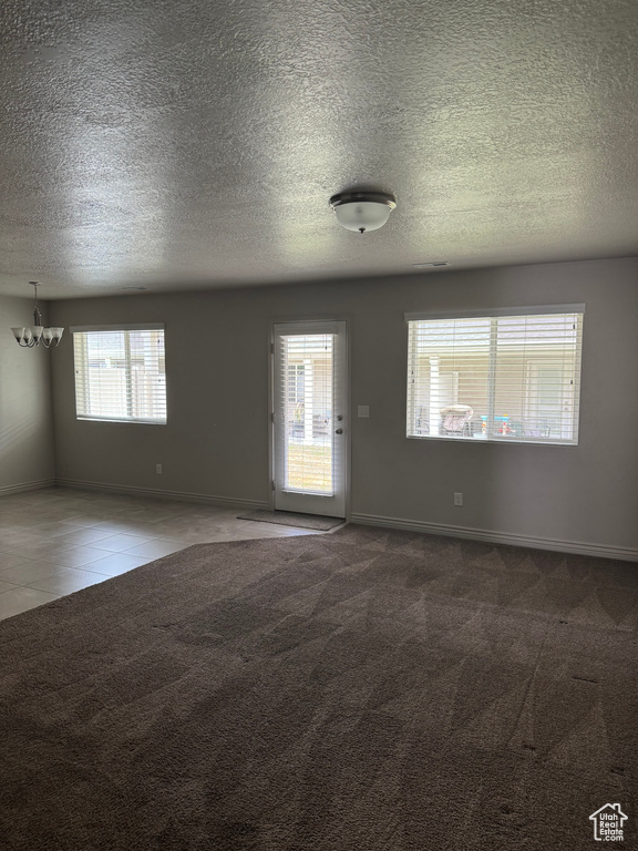 Carpeted spare room with plenty of natural light, an inviting chandelier, and a textured ceiling