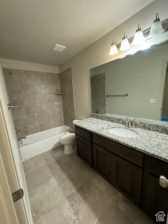 Full bathroom featuring a textured ceiling, tiled shower / bath combo, vanity, and toilet