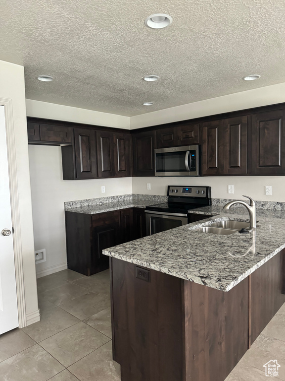 Kitchen with light stone counters, sink, kitchen peninsula, dark brown cabinets, and appliances with stainless steel finishes