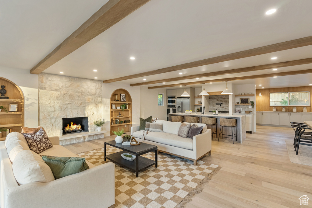 Living room with light hardwood / wood-style floors, beam ceiling, and a stone fireplace