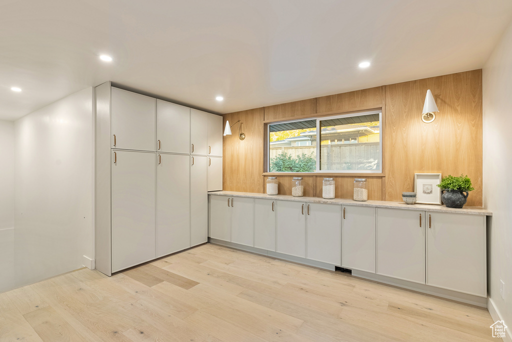 Kitchen featuring white cabinets, light wood-type flooring, and wood walls