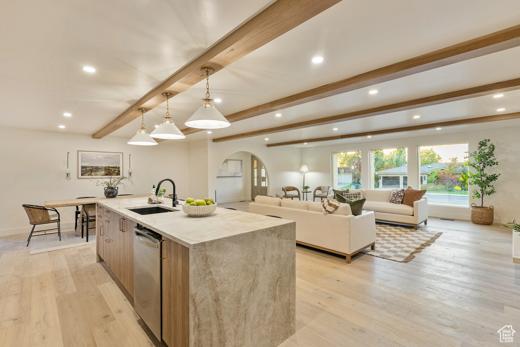 Kitchen with an island with sink, stainless steel dishwasher, sink, light hardwood / wood-style floors, and decorative light fixtures