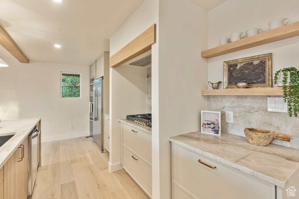 Kitchen featuring light stone counters, light wood-type flooring, backsplash, and stainless steel appliances