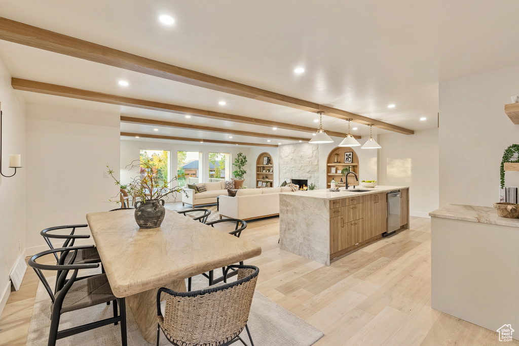 Kitchen featuring beamed ceiling, a fireplace, light hardwood / wood-style flooring, decorative light fixtures, and dishwasher