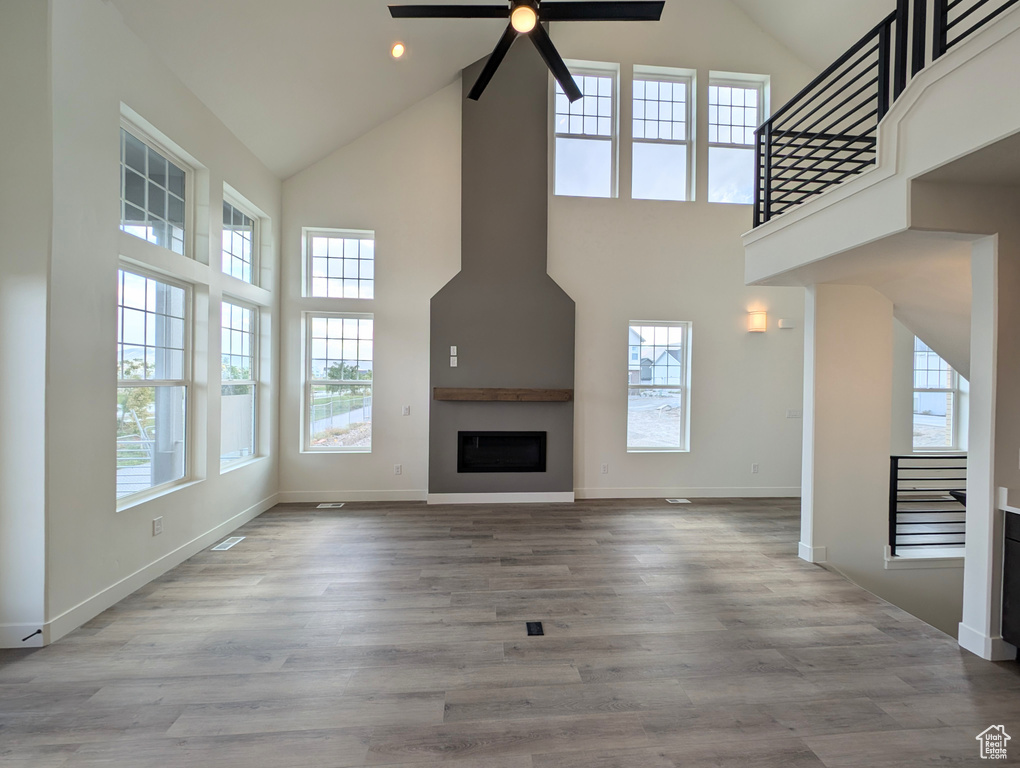 Unfurnished living room featuring a fireplace, high vaulted ceiling, light wood-type flooring, and ceiling fan