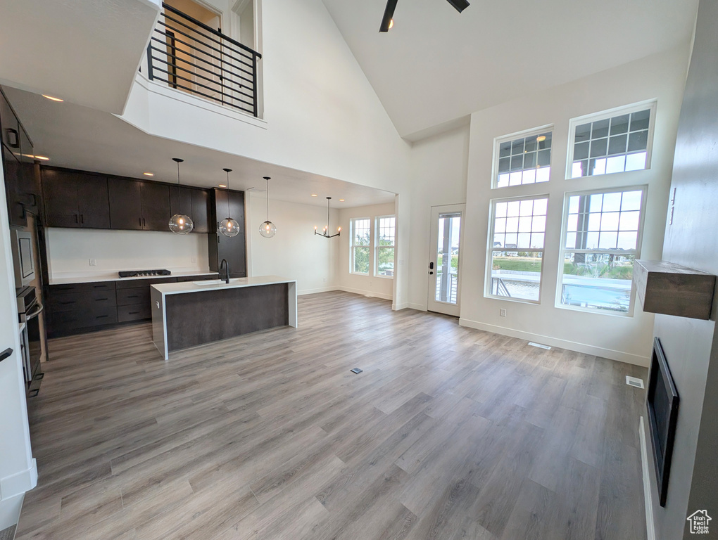 Unfurnished living room with a towering ceiling, ceiling fan with notable chandelier, hardwood / wood-style flooring, and sink