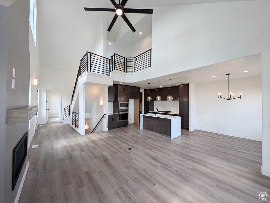 Unfurnished living room featuring ceiling fan with notable chandelier, hardwood / wood-style flooring, and a towering ceiling