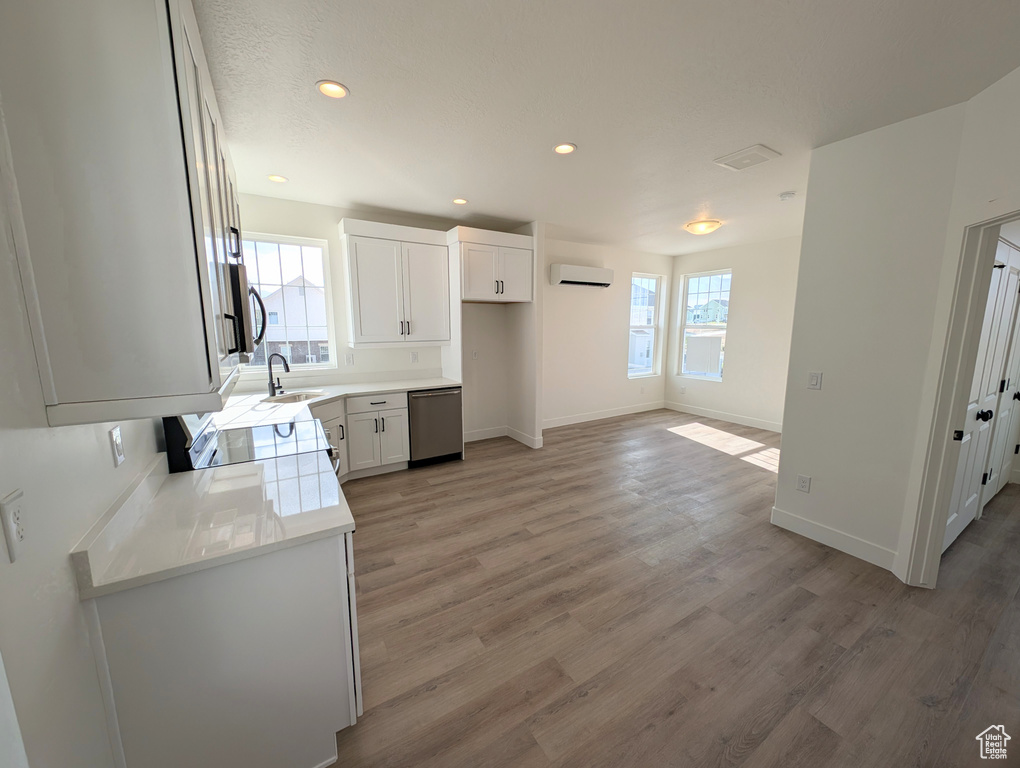 Kitchen with light wood-type flooring, a wall mounted air conditioner, sink, white cabinets, and appliances with stainless steel finishes