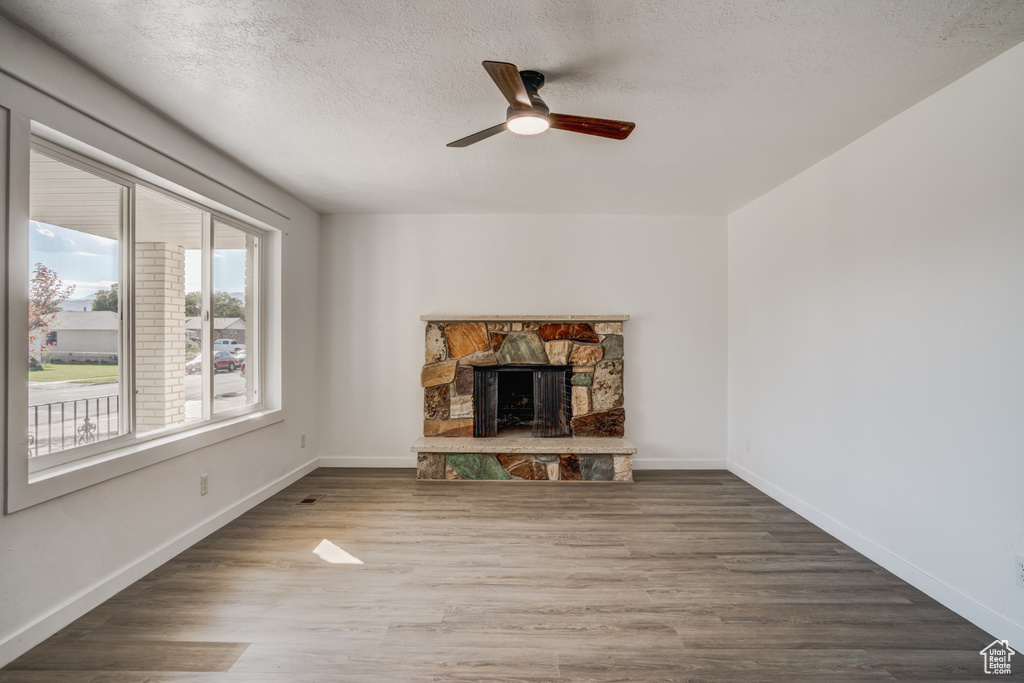 Unfurnished living room featuring a textured ceiling, wood-type flooring, a stone fireplace, and ceiling fan