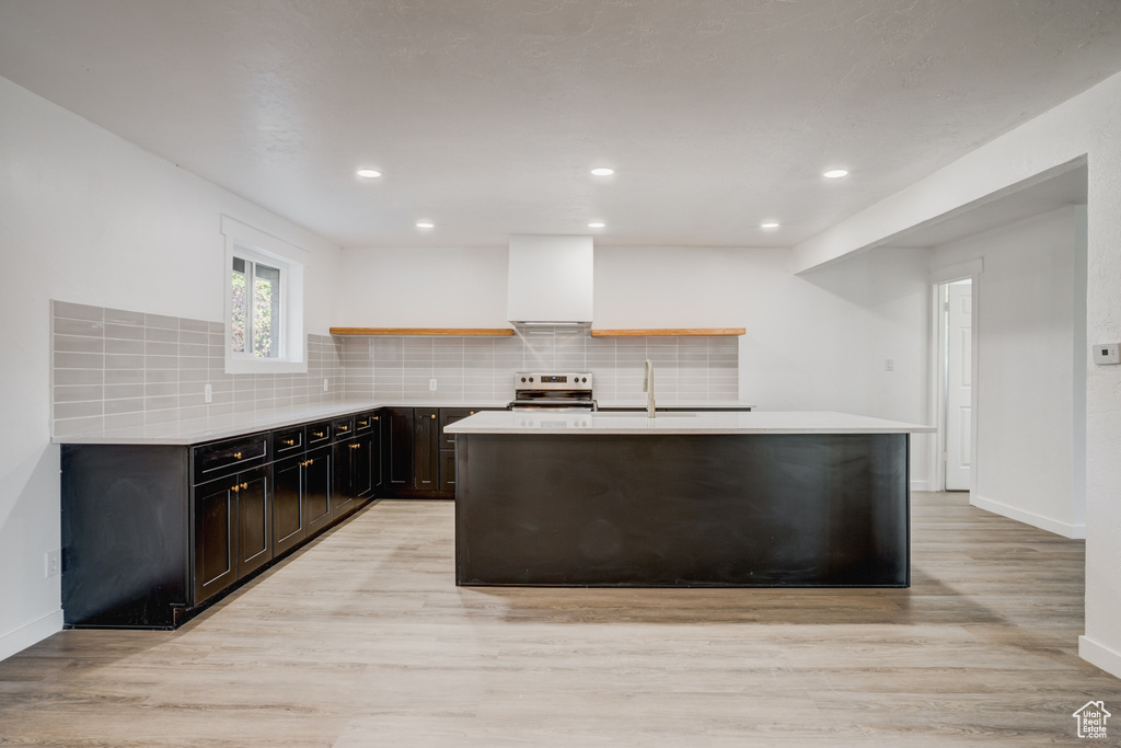 Kitchen with stainless steel electric stove, tasteful backsplash, light hardwood / wood-style flooring, a kitchen island with sink, and sink