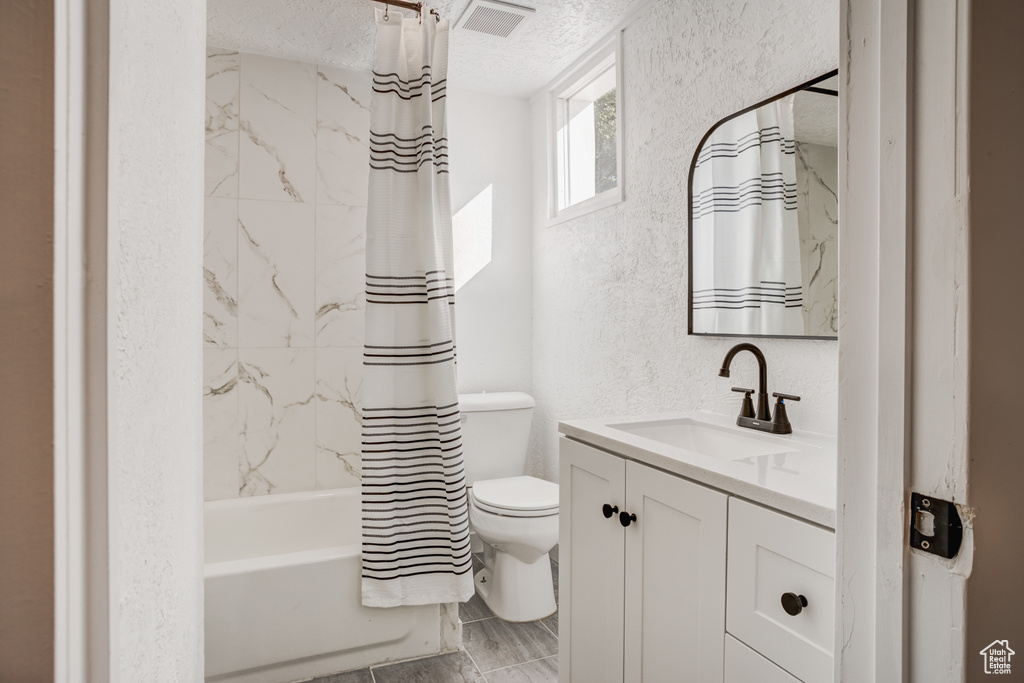 Full bathroom featuring vanity, shower / bath combo with shower curtain, toilet, and a textured ceiling