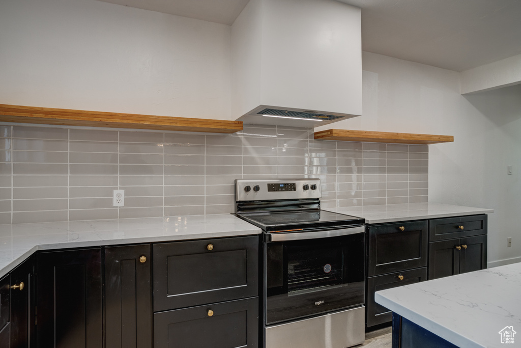 Kitchen with decorative backsplash, light stone countertops, stainless steel electric range oven, and extractor fan