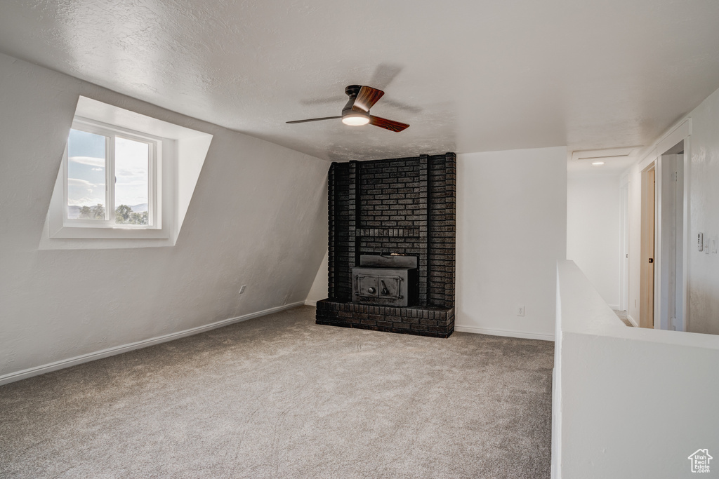 Unfurnished living room featuring ceiling fan, lofted ceiling, a wood stove, a textured ceiling, and carpet