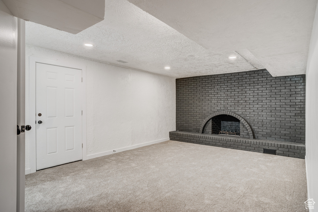 Unfurnished living room with a brick fireplace, brick wall, a textured ceiling, and carpet flooring