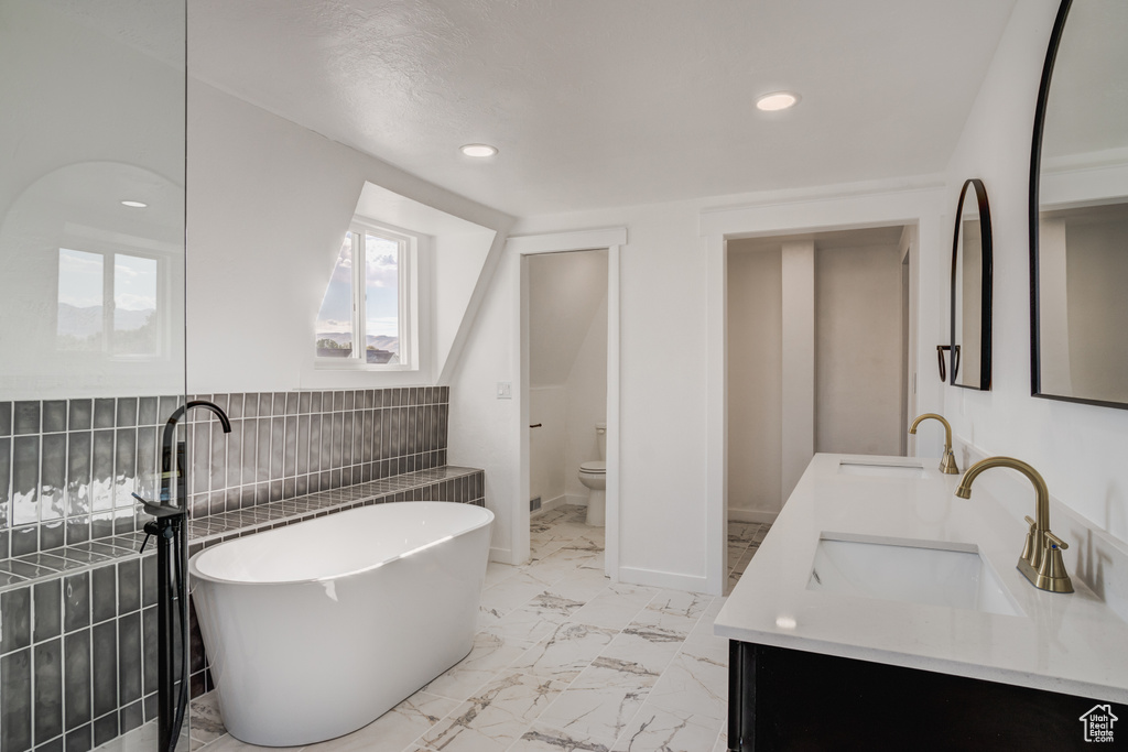 Bathroom with a tub to relax in, tile walls, vanity, and toilet