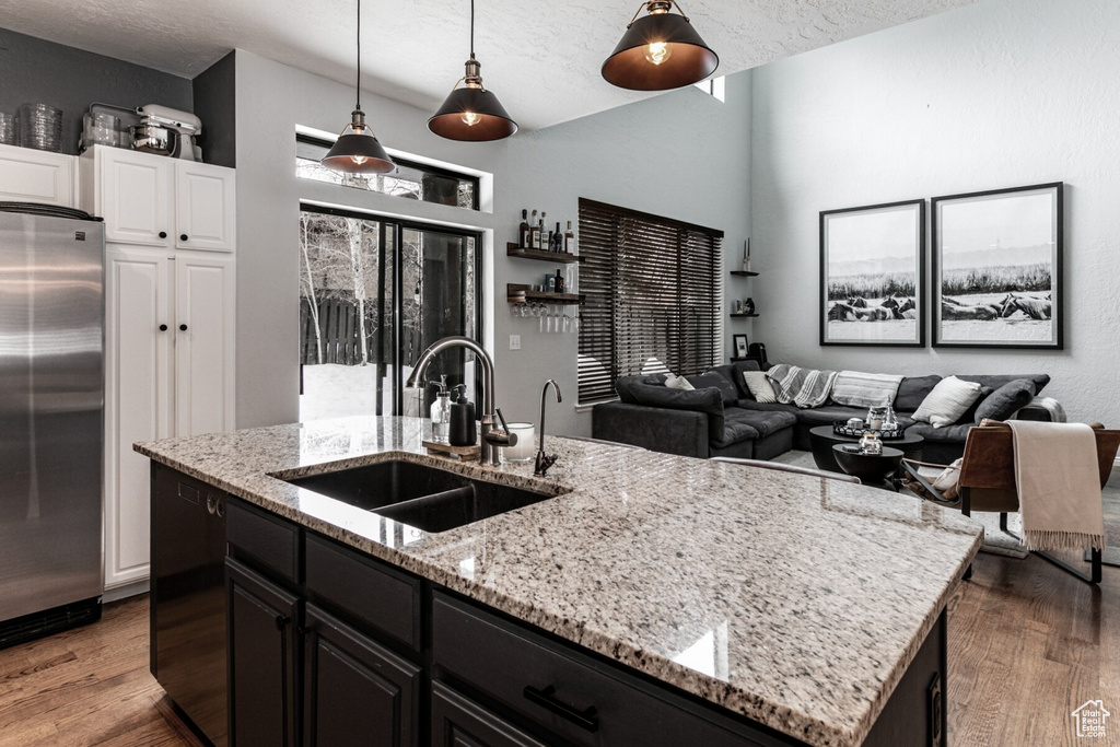 Kitchen with an island with sink, hanging light fixtures, stainless steel fridge, sink, and hardwood / wood-style floors