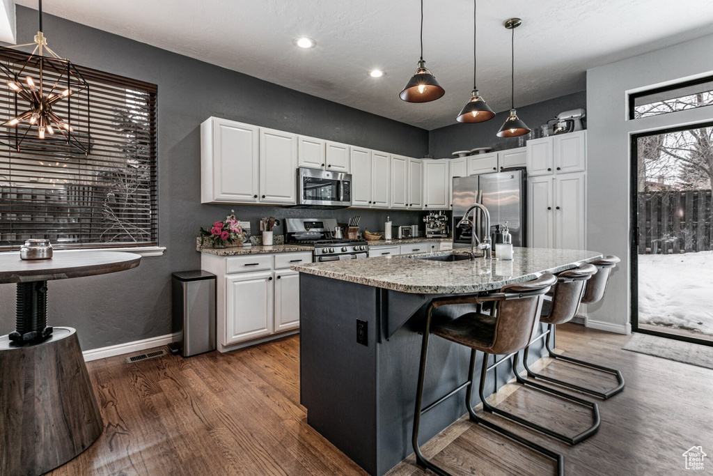 Kitchen featuring light stone countertops, an island with sink, appliances with stainless steel finishes, and white cabinetry