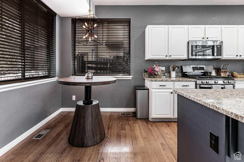 Kitchen featuring appliances with stainless steel finishes, pendant lighting, white cabinetry, and wood-type flooring