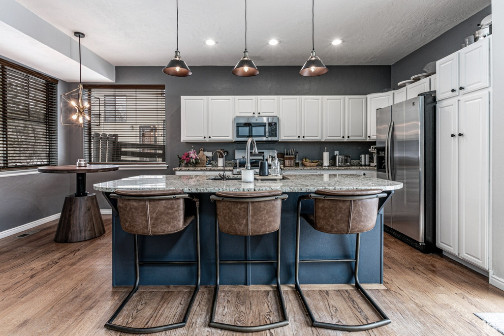 Kitchen with light stone countertops, white cabinetry, decorative light fixtures, and stainless steel appliances